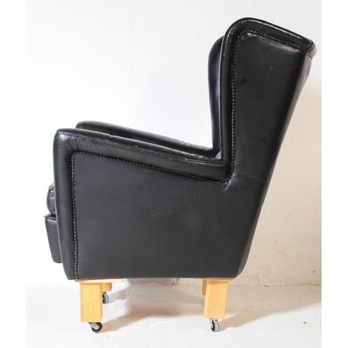 572 - G Plan - A mid 20th century G-Plan batwing black faux leatherette vinyl armchair being raised on lat... 