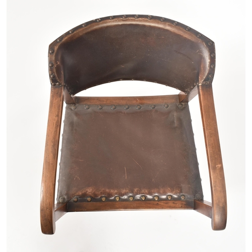 192 - An early 20th century Arts & Crafts oak and leather elbow chair. The chair having a curved leather u... 