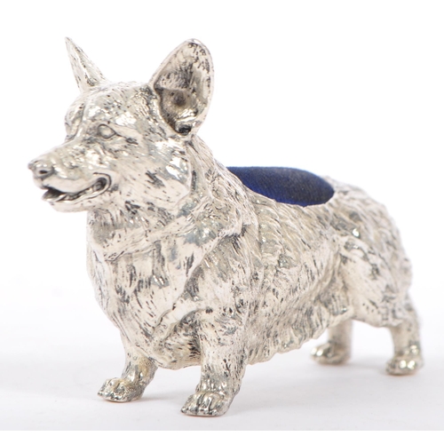 366 - A silver plated pin cushion in the form of a corgi dog having engraved features to body with blue cu... 