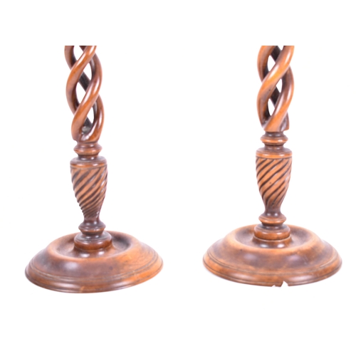 23 - A pair of early 20th century mahogany open barley twist stemmed candlesticks. Each with brass cupped... 