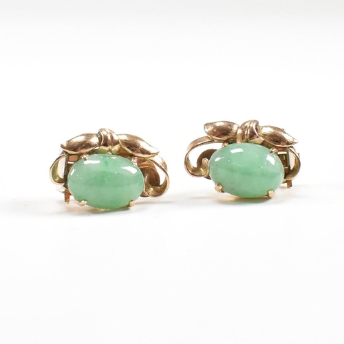 135 - A pair of mid century gold and jade ear clip earrings. The earrings set with jade cabochons. Unmarke... 