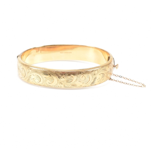 423 - A hallmarked 9ct gold hinged bangle. The bangle having etched foliate decoration and safety chain. H... 