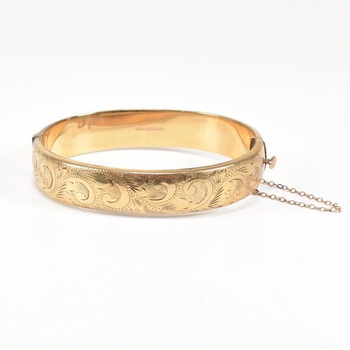 423 - A hallmarked 9ct gold hinged bangle. The bangle having etched foliate decoration and safety chain. H... 