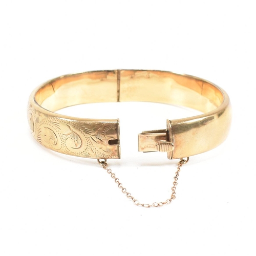 423 - A hallmarked 9ct gold hinged bangle. The bangle having etched foliate decoration and safety chain. H... 