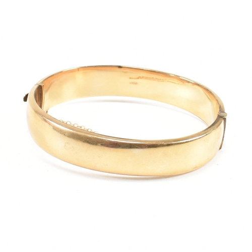 423 - A hallmarked 9ct gold hinged bangle. The bangle having etched foliate decoration and safety chain. H... 