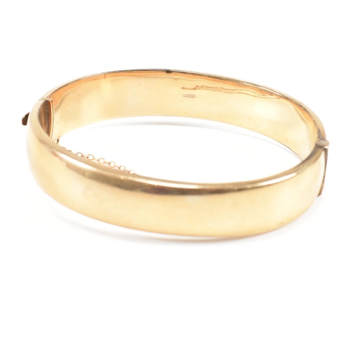 423 - A hallmarked 9ct gold hinged bangle. The bangle having etched foliate decoration and safety chain. H... 