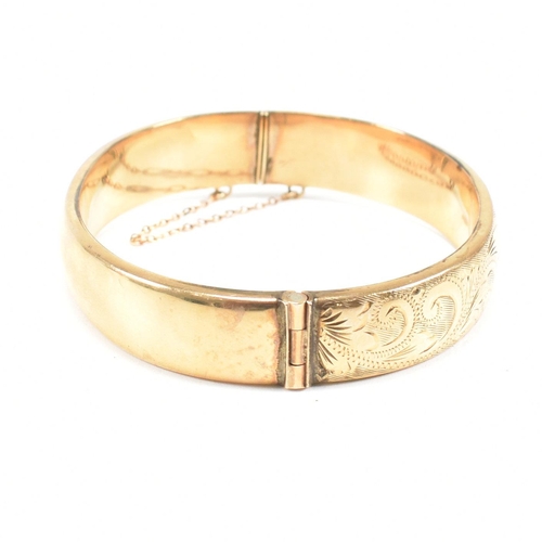 423 - A hallmarked 9ct gold hinged bangle. The bangle having etched foliate decoration and safety chain. H... 