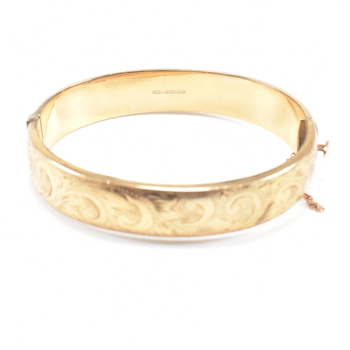 423 - A hallmarked 9ct gold hinged bangle. The bangle having etched foliate decoration and safety chain. H... 