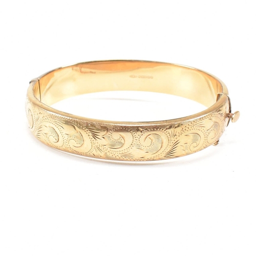 423 - A hallmarked 9ct gold hinged bangle. The bangle having etched foliate decoration and safety chain. H... 