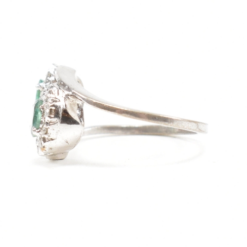 457 - A white gold emerald and diamond crossover ring. The ring set with two oval cut emeralds each framed... 