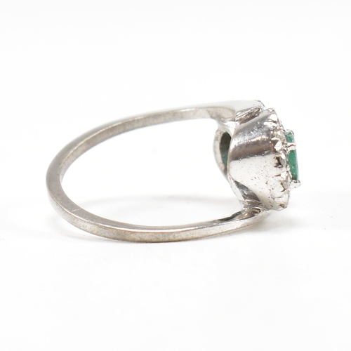 457 - A white gold emerald and diamond crossover ring. The ring set with two oval cut emeralds each framed... 