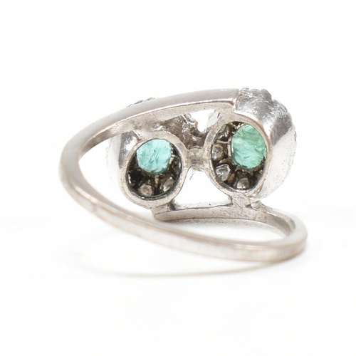 457 - A white gold emerald and diamond crossover ring. The ring set with two oval cut emeralds each framed... 