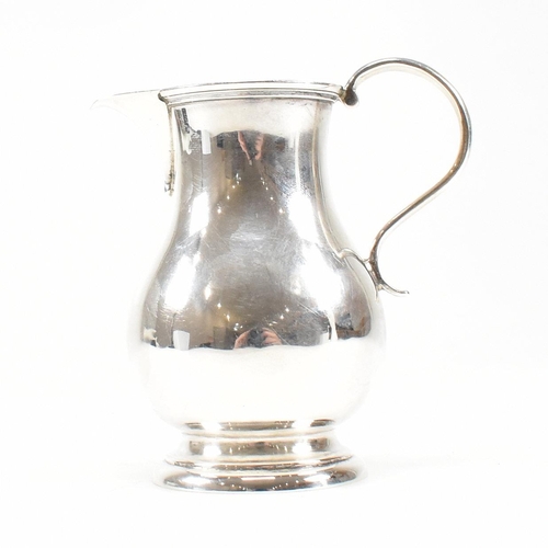 175 - A Victorian hallmarked silver creamer jug. The jug on a round foot rising to baluster body with scro... 