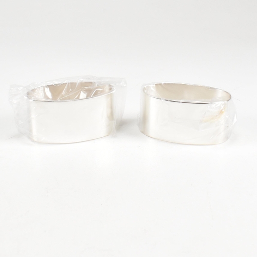 43 - A 1990s pair of cased hallmarked silver napkin rings. The napkin rings of oblong form and having ori... 