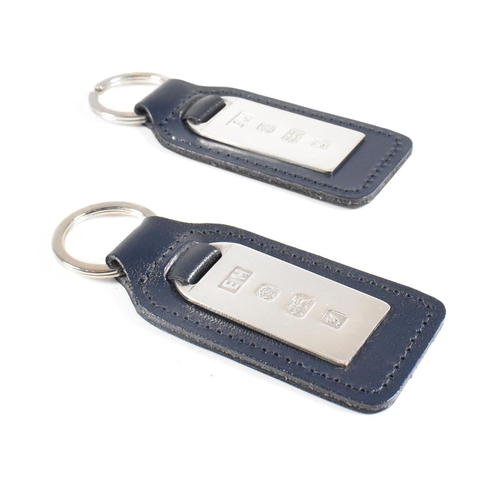 55 - Two 1990s hallmarked silver and leather tag keyrings. The silver tags backed with navy blue leather ... 