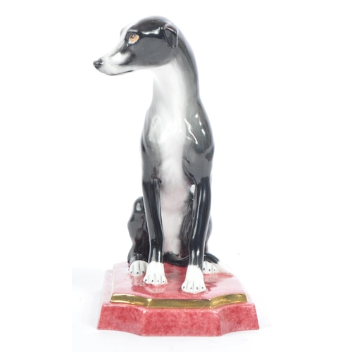 129 - Halcyon Days - A vintage 20th century porcelain figure of a Greyhound dog. In a seat position in a b... 