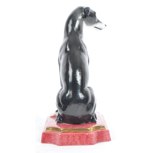 129 - Halcyon Days - A vintage 20th century porcelain figure of a Greyhound dog. In a seat position in a b... 