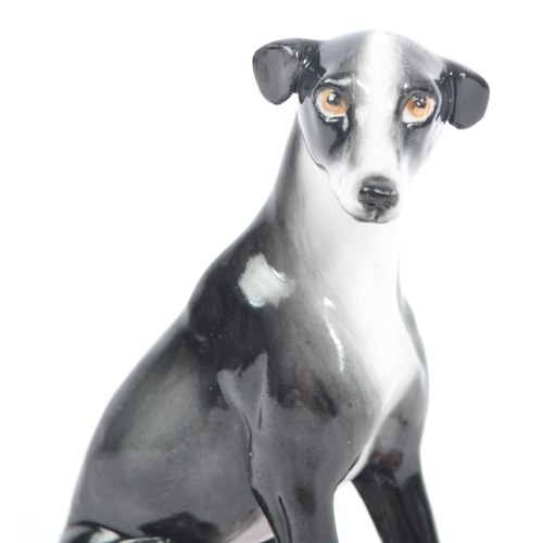 129 - Halcyon Days - A vintage 20th century porcelain figure of a Greyhound dog. In a seat position in a b... 