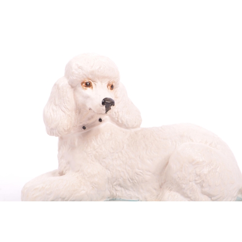 149 - Beswick - A late 20th matte finish white Beswick poodle seated on a blue cushion with yellow trim. M... 