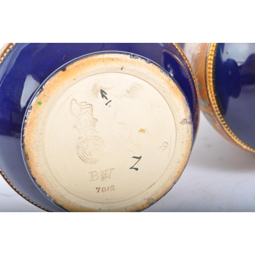 123 - A pair of Royal Doulton Lambeth stem vases. Having a flared blue rim into a tapering neck, with the ... 