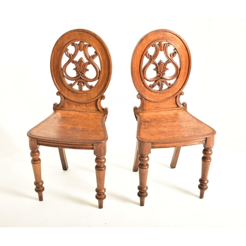 443 - A pair of Victorian 19th century carved oak round back hall chairs. Each chair having a pierced roun... 