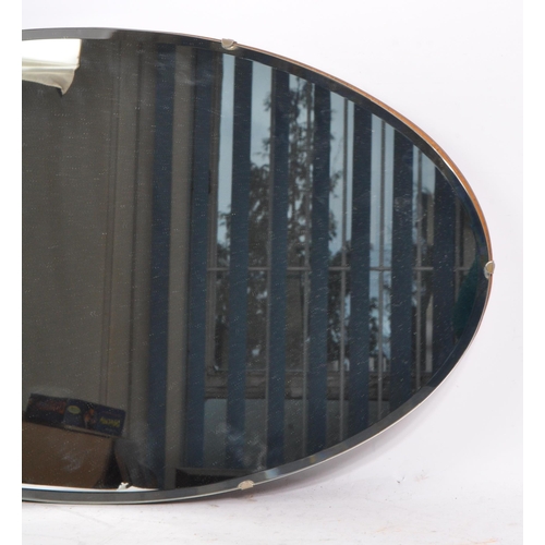 784 - A 1940s mid 20th century frameless oval bevelled edge wall hanging mirror. Having mahogany wood back... 