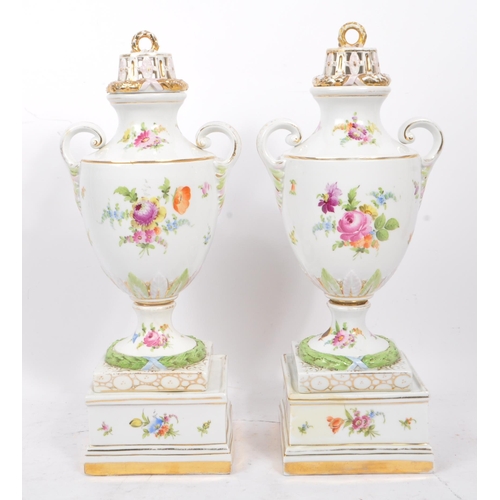 122 - A pair of china porcelain continental Dresden spray style twin handle lidded urns upon a square form... 