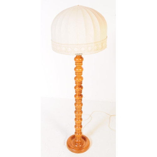 575 - A contemporary blond wood floor standing lamp. The lamp having turned column with bulbous repeating ... 