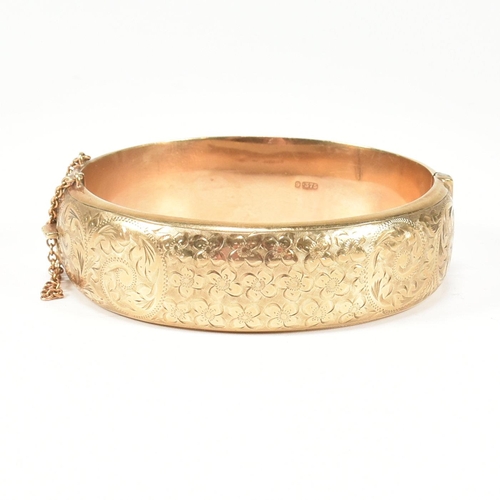 113 - A hallmarked 9ct gold hinged bangle. The gold bangle having bright cut engraved floral decoration to... 