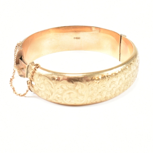 113 - A hallmarked 9ct gold hinged bangle. The gold bangle having bright cut engraved floral decoration to... 