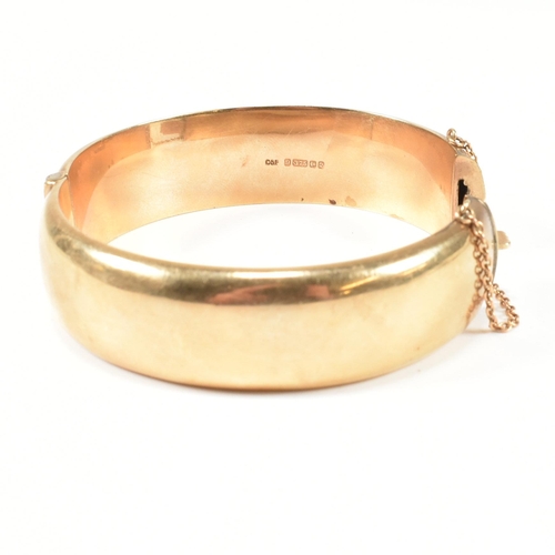 113 - A hallmarked 9ct gold hinged bangle. The gold bangle having bright cut engraved floral decoration to... 