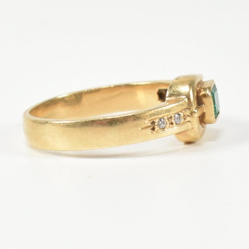 148 - An 18ct gold, diamond and emerald buckle ring. The gold buckle ring having a bezel set east-west eme... 