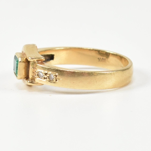 148 - An 18ct gold, diamond and emerald buckle ring. The gold buckle ring having a bezel set east-west eme... 