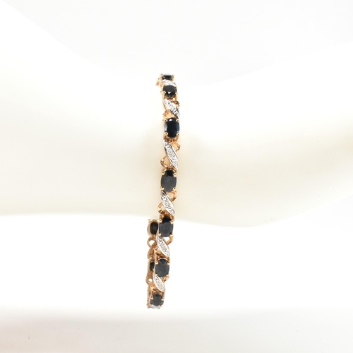 218 - A 9ct gold, sapphire and diamond line bracelet. The bracelet having fourteen oval cut sapphires inte... 