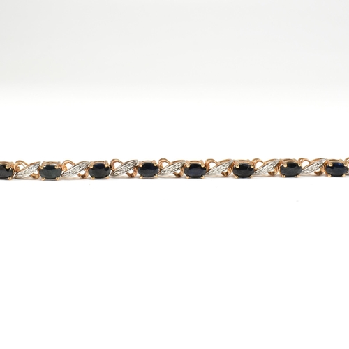 218 - A 9ct gold, sapphire and diamond line bracelet. The bracelet having fourteen oval cut sapphires inte... 