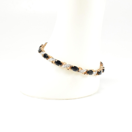 218 - A 9ct gold, sapphire and diamond line bracelet. The bracelet having fourteen oval cut sapphires inte... 