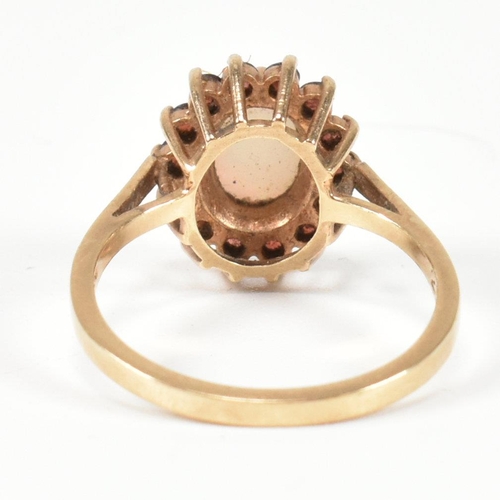 225 - A hallmarked 9ct gold, opal and red stone cluster ring. The ring having a central oval opal cabochon... 