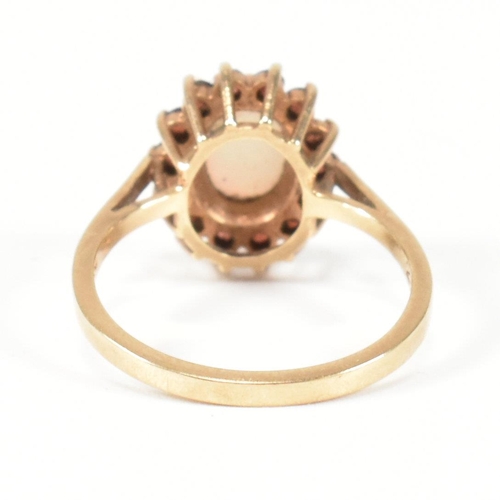 225 - A hallmarked 9ct gold, opal and red stone cluster ring. The ring having a central oval opal cabochon... 