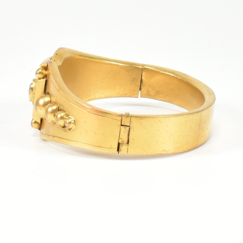 267 - A 19th century Etruscan style gilt hanged bangle. The bangle having a central paste set cross motif ... 