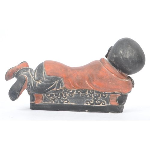 33 - An early 20th Century Chinese ceramic / clay pillow in the form of a lounging Buddha like / baby fig... 