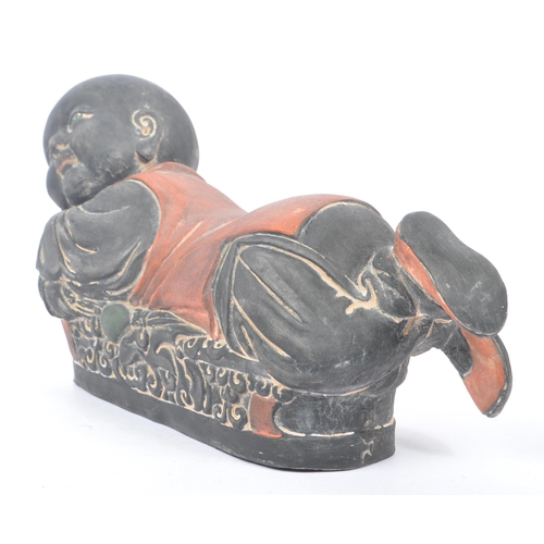 33 - An early 20th Century Chinese ceramic / clay pillow in the form of a lounging Buddha like / baby fig... 