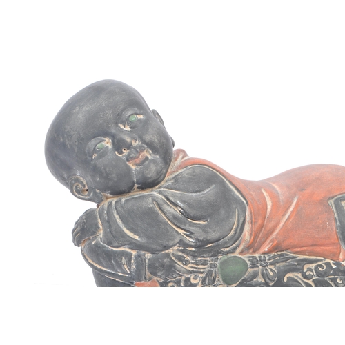 33 - An early 20th Century Chinese ceramic / clay pillow in the form of a lounging Buddha like / baby fig... 