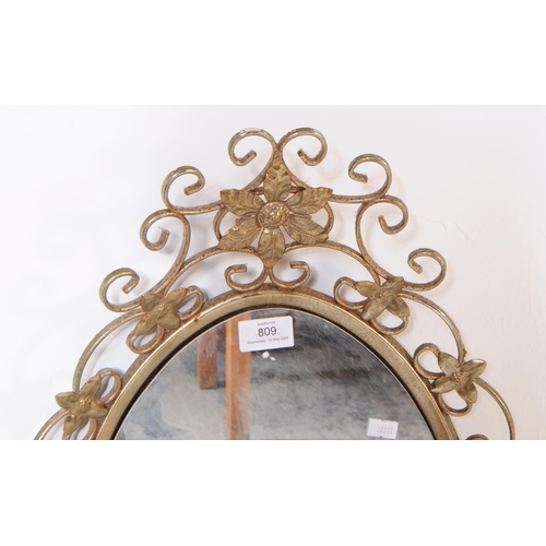 809 - A mid 20th century brass framed wall mirror. The mirror having scrolled metal work frame, with flora... 