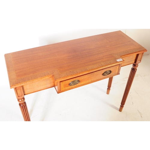 976 - A Sheraton revival mahogany breakfront writing table having reeded legs and cross banded top with bo... 