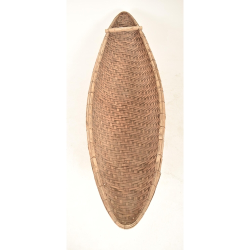 353 - A large African tribal hand woven wicker rattan canoe shaped cot / basket. The basket having a reinf... 