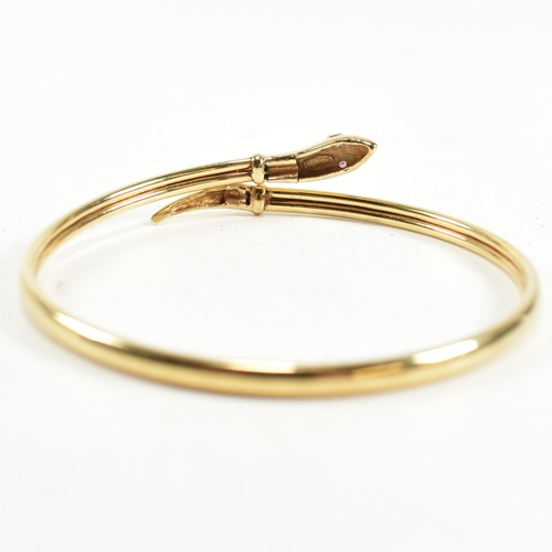 108 - A 9ct gold and ruby snake bangle. The snake bangle having a wrap-around design with the snake head a... 