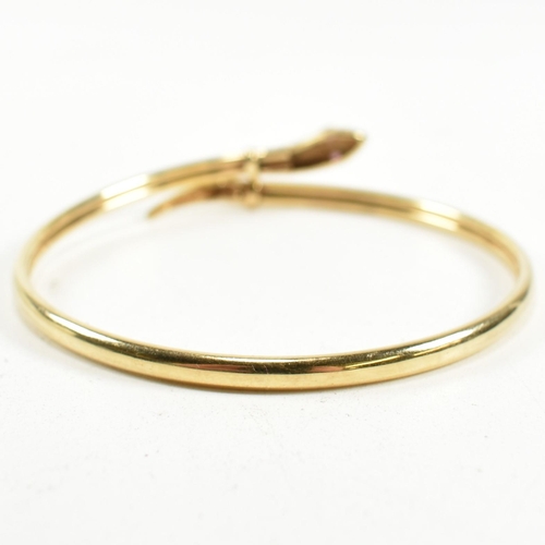 108 - A 9ct gold and ruby snake bangle. The snake bangle having a wrap-around design with the snake head a... 