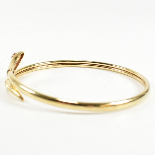 108 - A 9ct gold and ruby snake bangle. The snake bangle having a wrap-around design with the snake head a... 