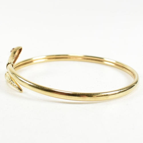 108 - A 9ct gold and ruby snake bangle. The snake bangle having a wrap-around design with the snake head a... 