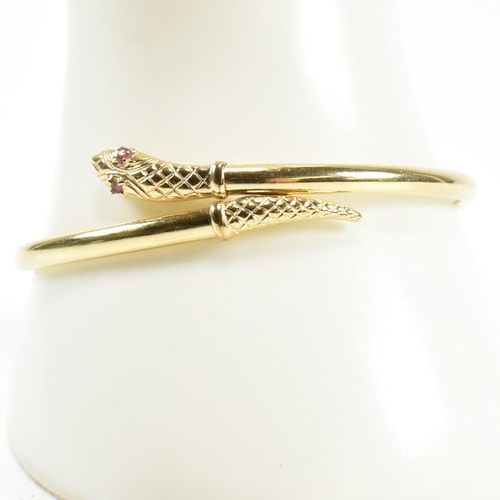 108 - A 9ct gold and ruby snake bangle. The snake bangle having a wrap-around design with the snake head a... 